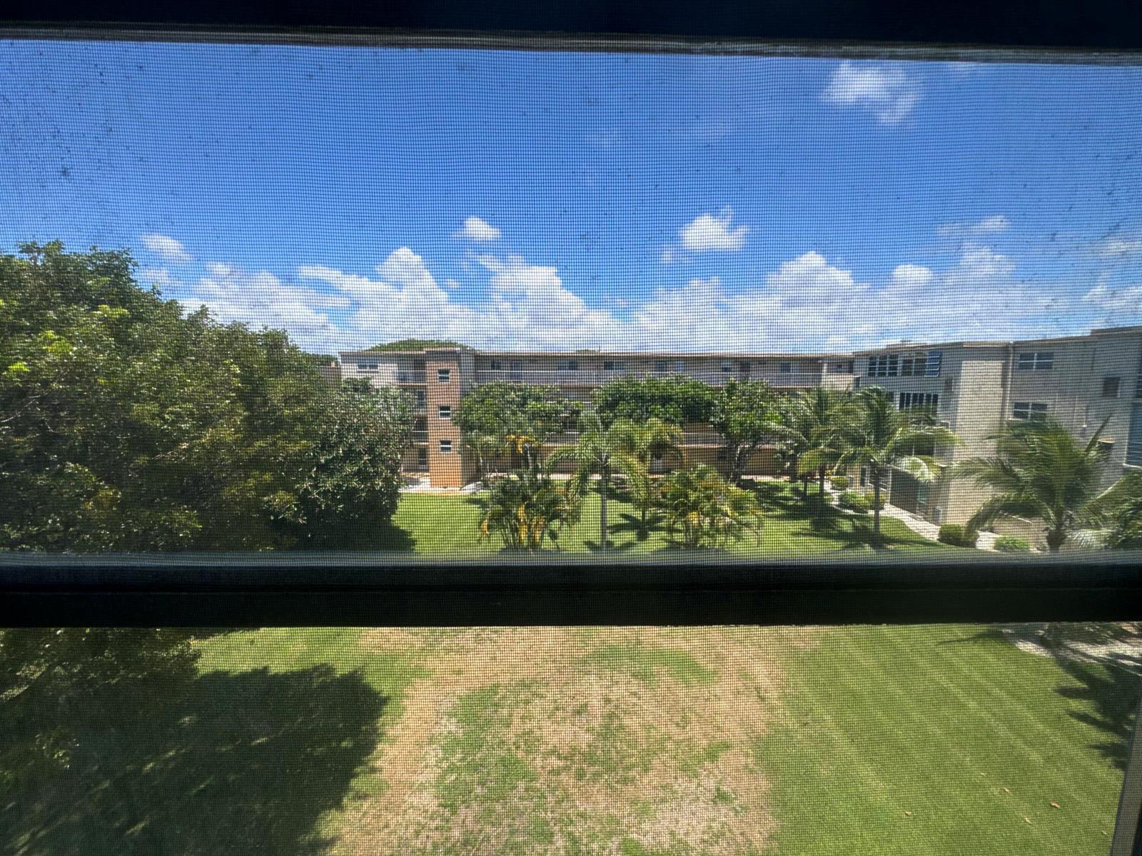 A view from a window looking out over a grassy courtyard and apartment buildings — 2615 NE 3rd Court # 4120, Boynton Beach FL 33435, BOYNTON BEACH, FL