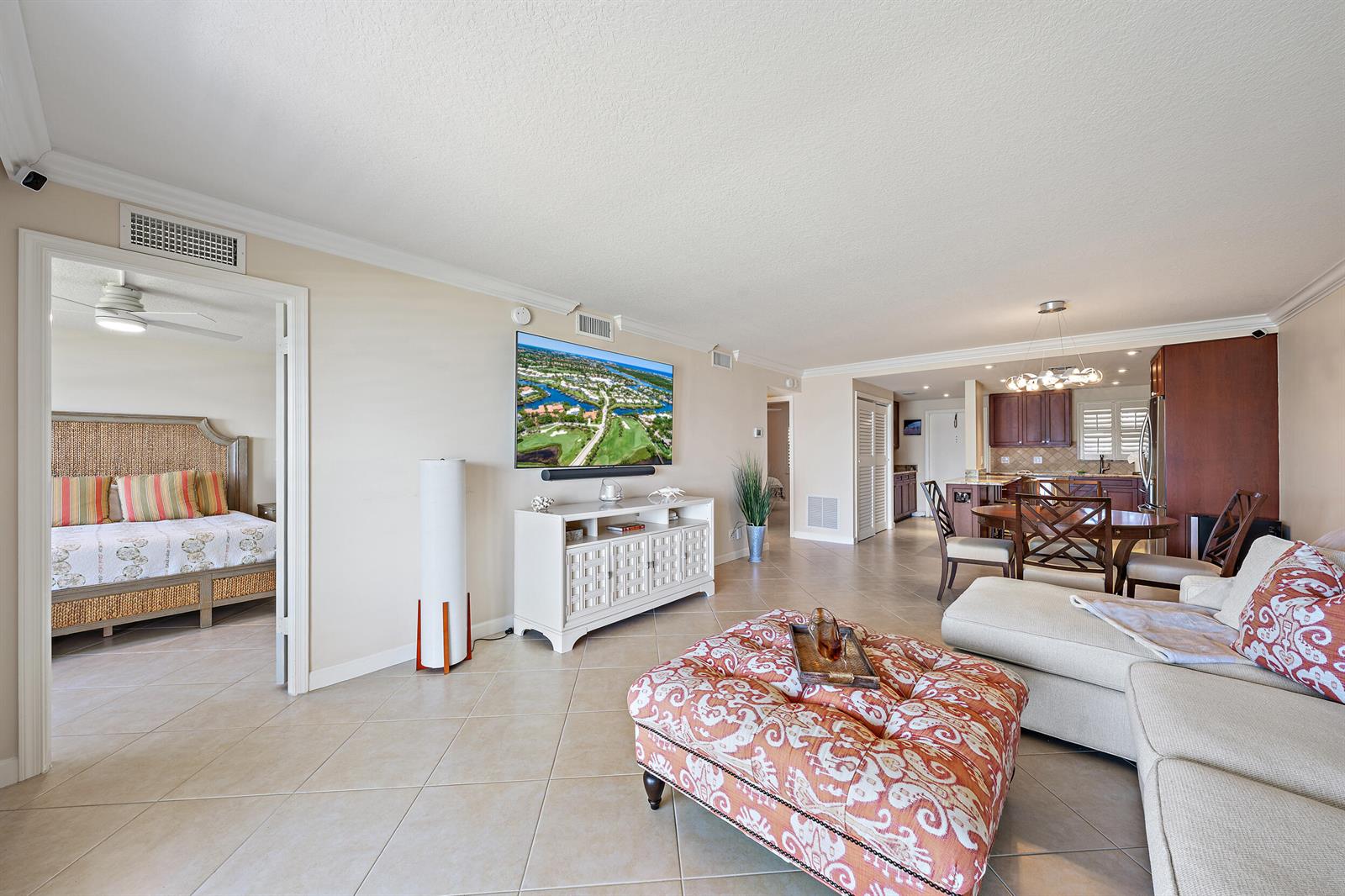 An open-concept living room features tile flooring, a large television, and an adjacent kitchen — 1051 Sugar Sands Boulevard # 156, Singer Island FL 33404, SINGER ISLAND, FL