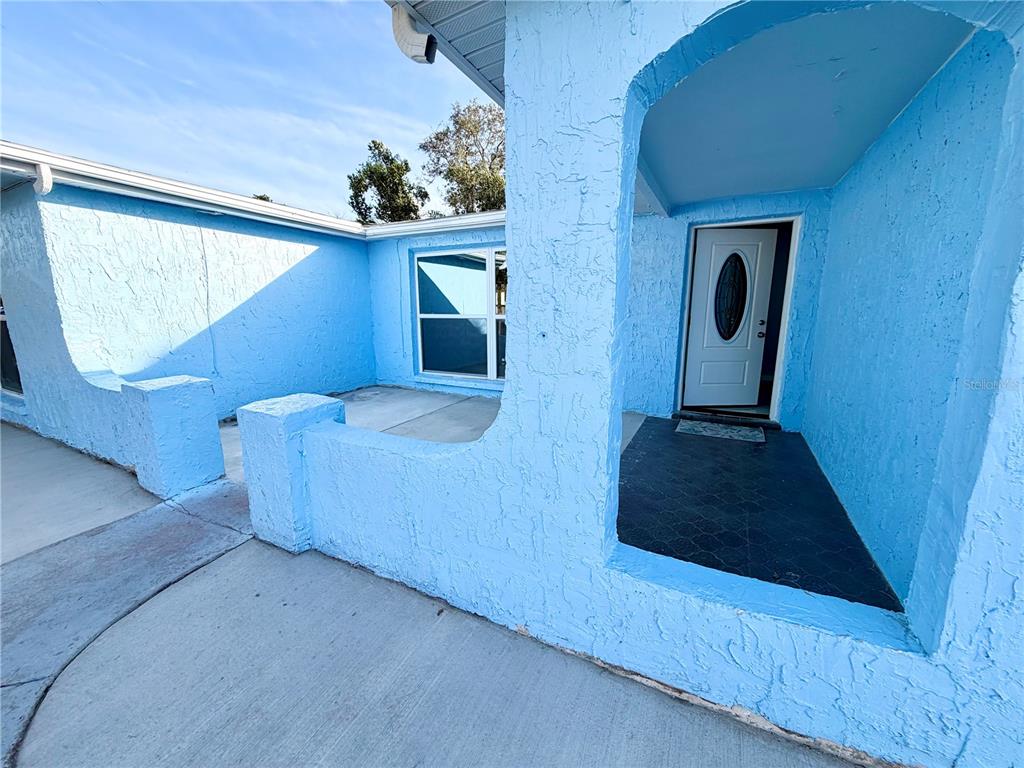 A bright blue stucco exterior features a covered entryway and a white front door — 7040 FOX HOLLOW DRIVE, PORT RICHEY, FL