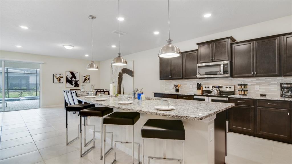 A kitchen features dark wood cabinets, granite countertops, a large island, and stainless steel appliances — 3005 MAHALO DRIVE, DAVENPORT, FL