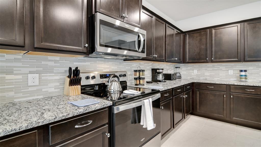 A kitchen features dark wood cabinets, granite countertops, stainless steel appliances, and a tiled backsplash — 3005 MAHALO DRIVE, DAVENPORT, FL