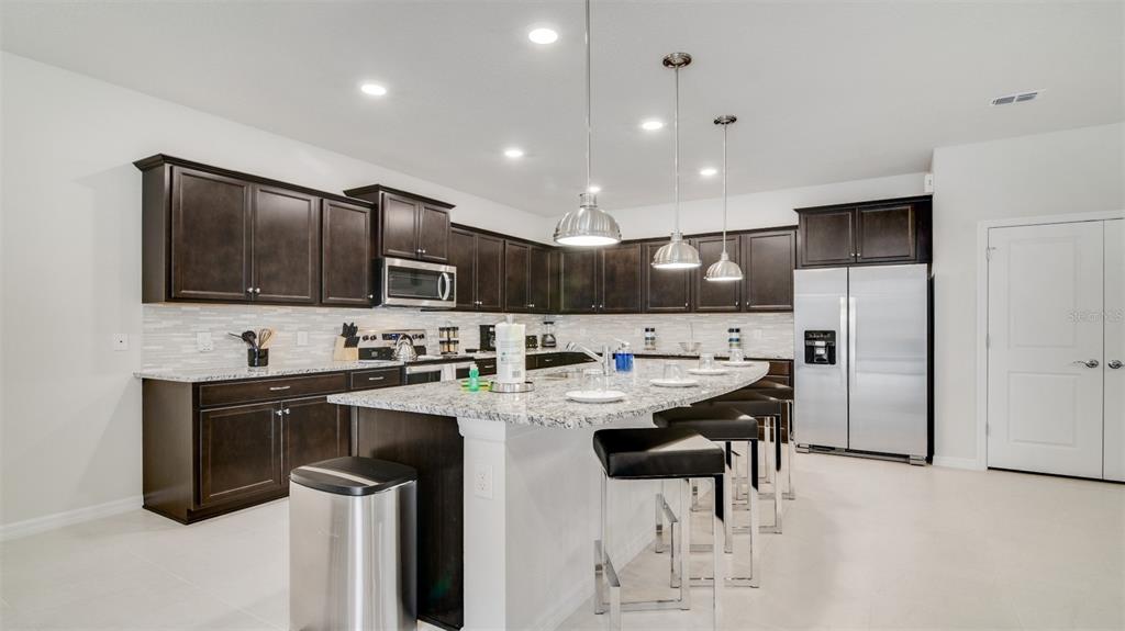 A kitchen features dark wood cabinets, granite countertops, a central island, and stainless steel appliances — 3005 MAHALO DRIVE, DAVENPORT, FL