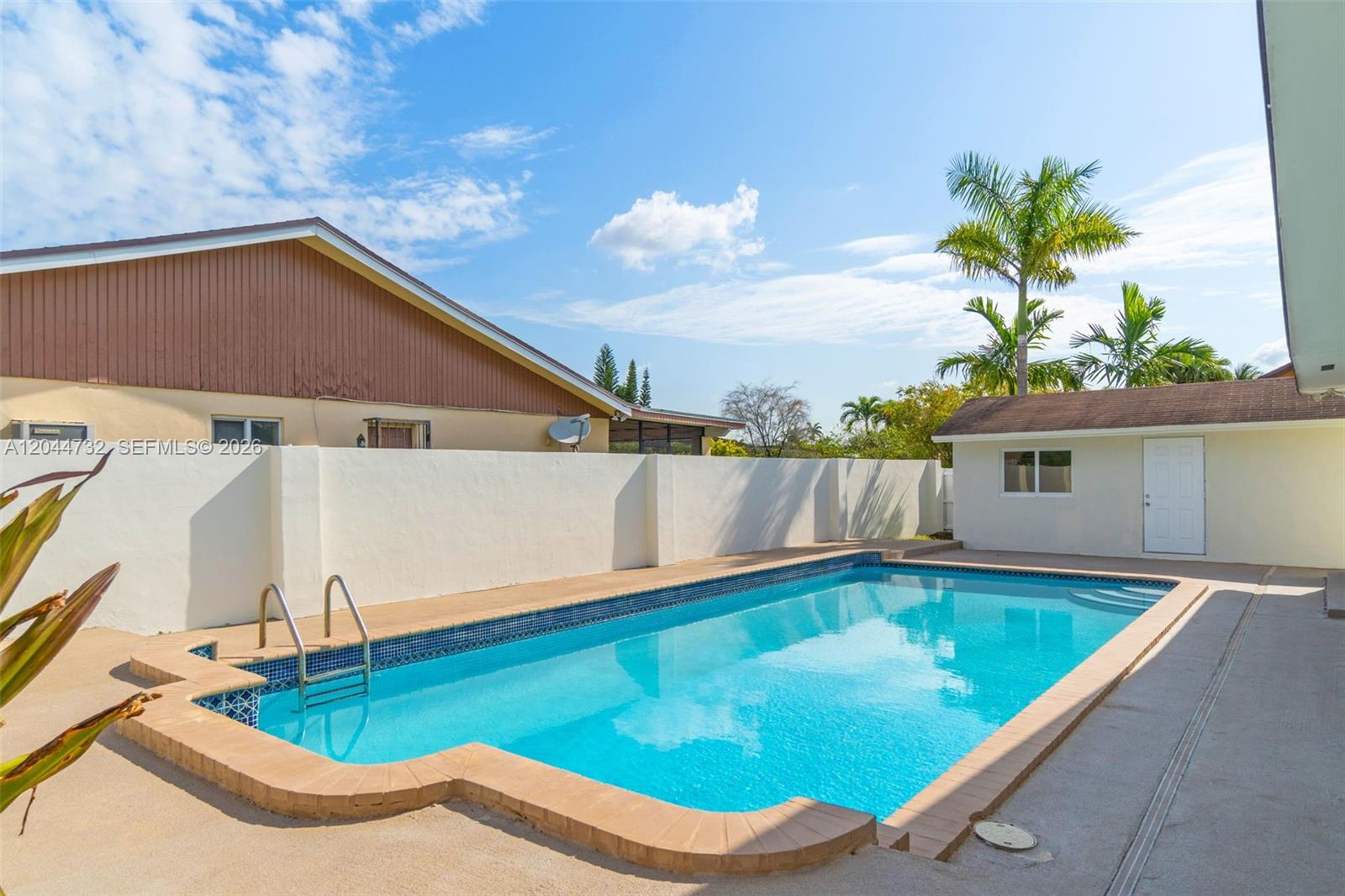 An outdoor swimming pool with a tan brick border sits in a fenced backyard — 7125 SW 93rd Ct, Miami FL 33173, MIAMI, FL