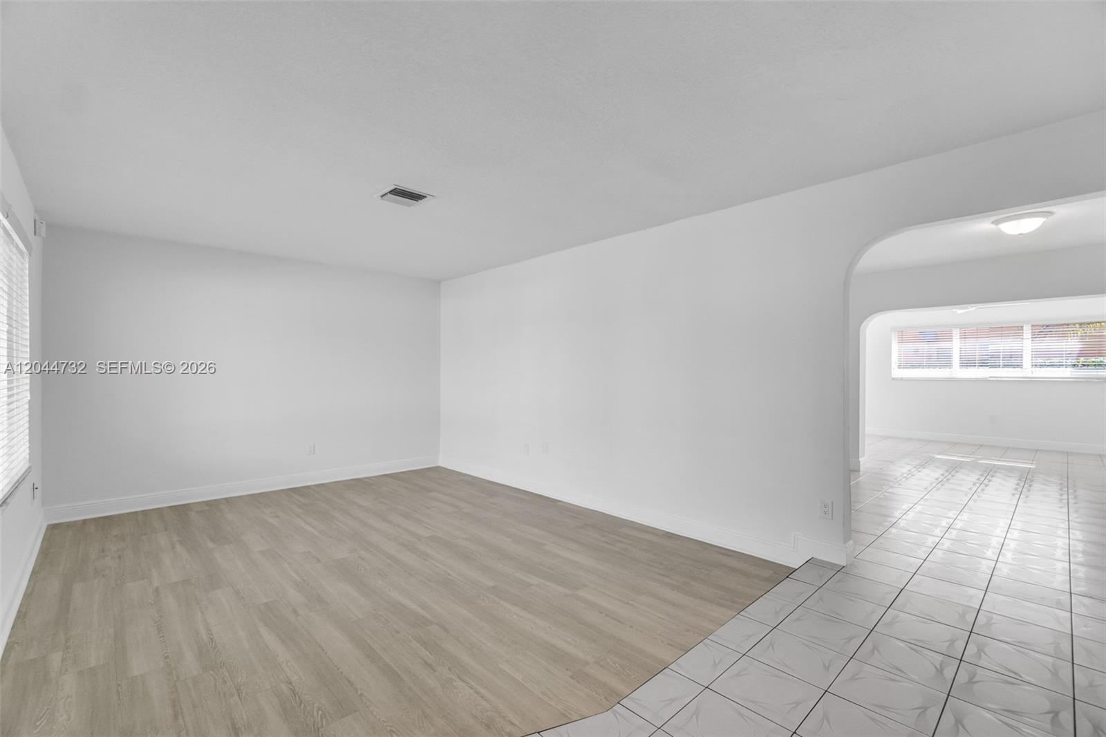 An empty room features light wood-look flooring, white walls, and an arched entryway to another room — 7125 SW 93rd Ct, Miami FL 33173, MIAMI, FL