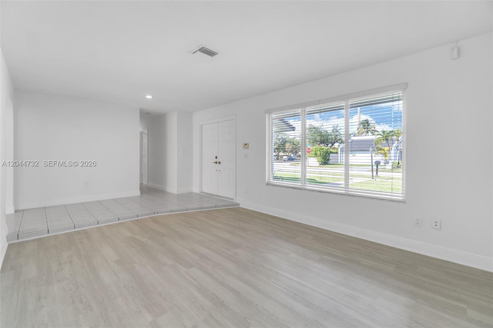 A bright, empty living room features light wood-look flooring, white walls, and a large window — 7125 SW 93rd Ct, Miami FL 33173, MIAMI, FL