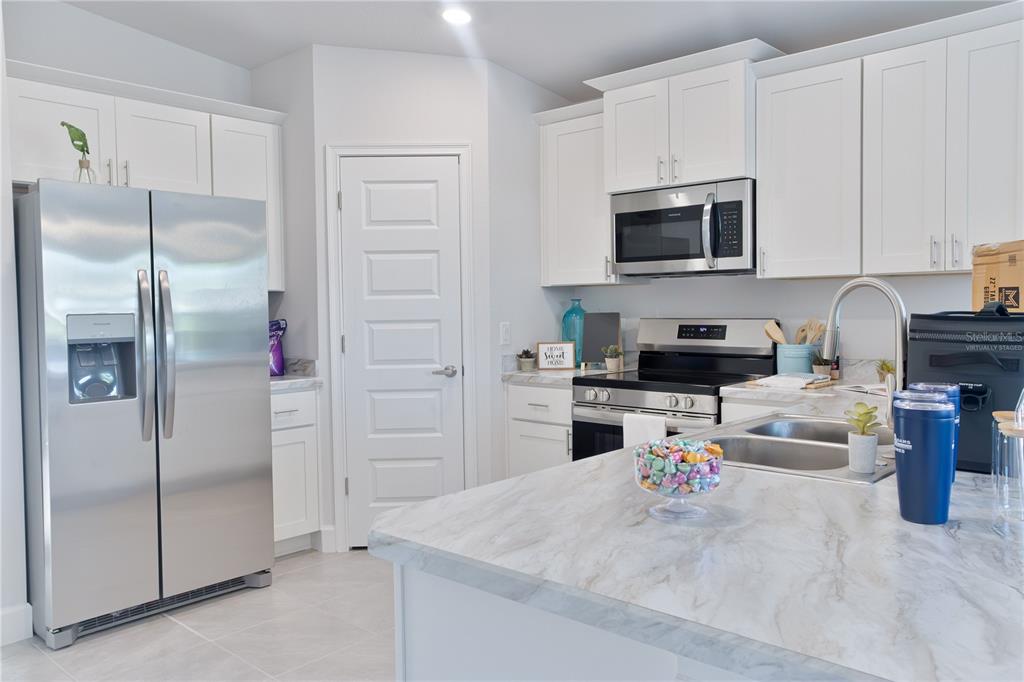 A modern kitchen features white cabinets, stainless steel appliances, and a marble-patterned island countertop — 1841 N ROBERTS TRAIL, BELL, FL