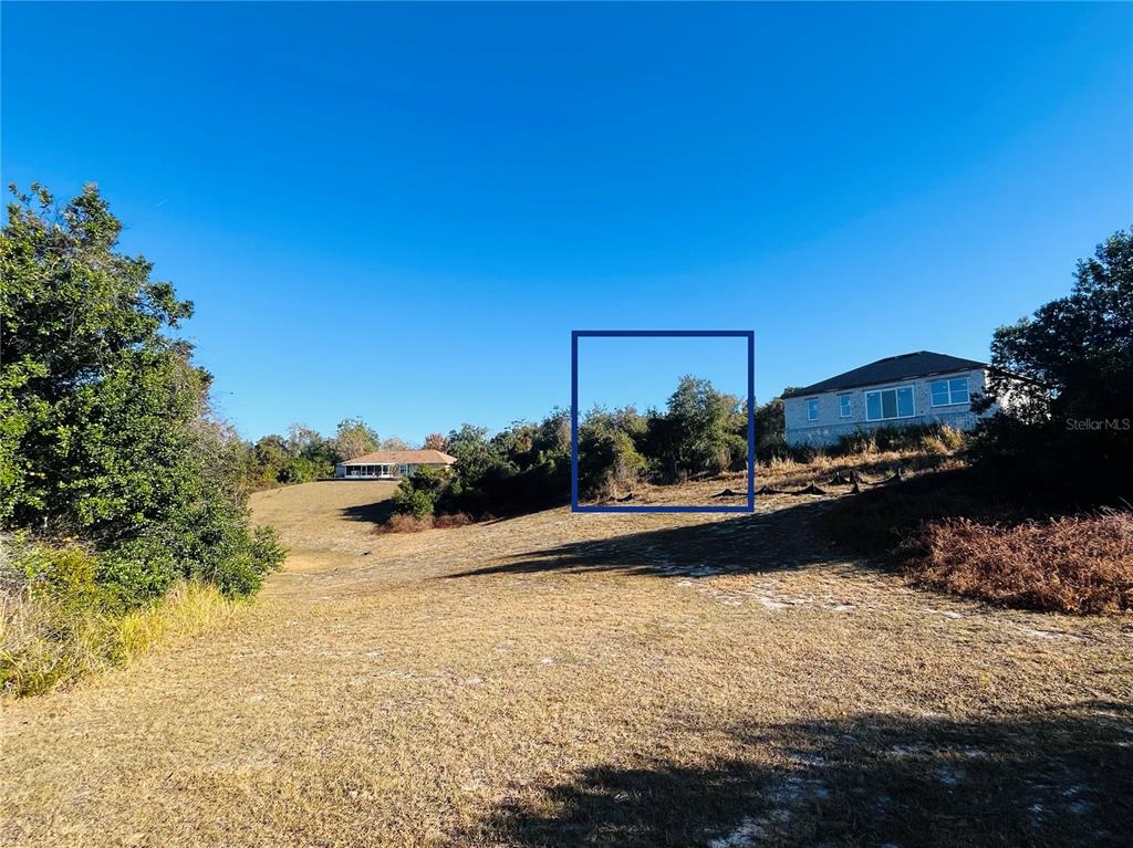 A grassy, sloped lot features a blue box highlighting a wooded area between two houses — 2106 E GLORIA DRIVE, DELTONA, FL