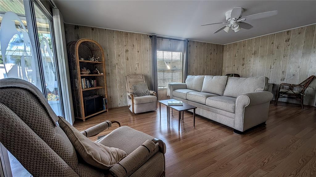 A living room features wood-paneled walls, wood flooring, a gray sofa, and a ceiling fan — 39820 US HIGHWAY 19 N UNIT 199, TARPON SPRINGS, FL