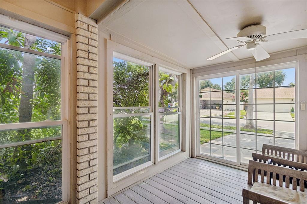 A sunroom with white brick accents, large windows, a ceiling fan, and wooden flooring — 5485 FRIARSWAY DRIVE, TAMPA, FL