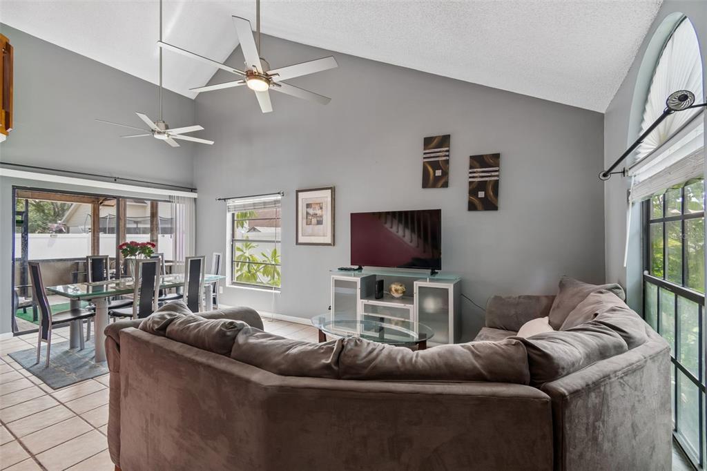 A living room with a vaulted ceiling, ceiling fans, tile floors, and a sectional sofa — 5485 FRIARSWAY DRIVE, TAMPA, FL