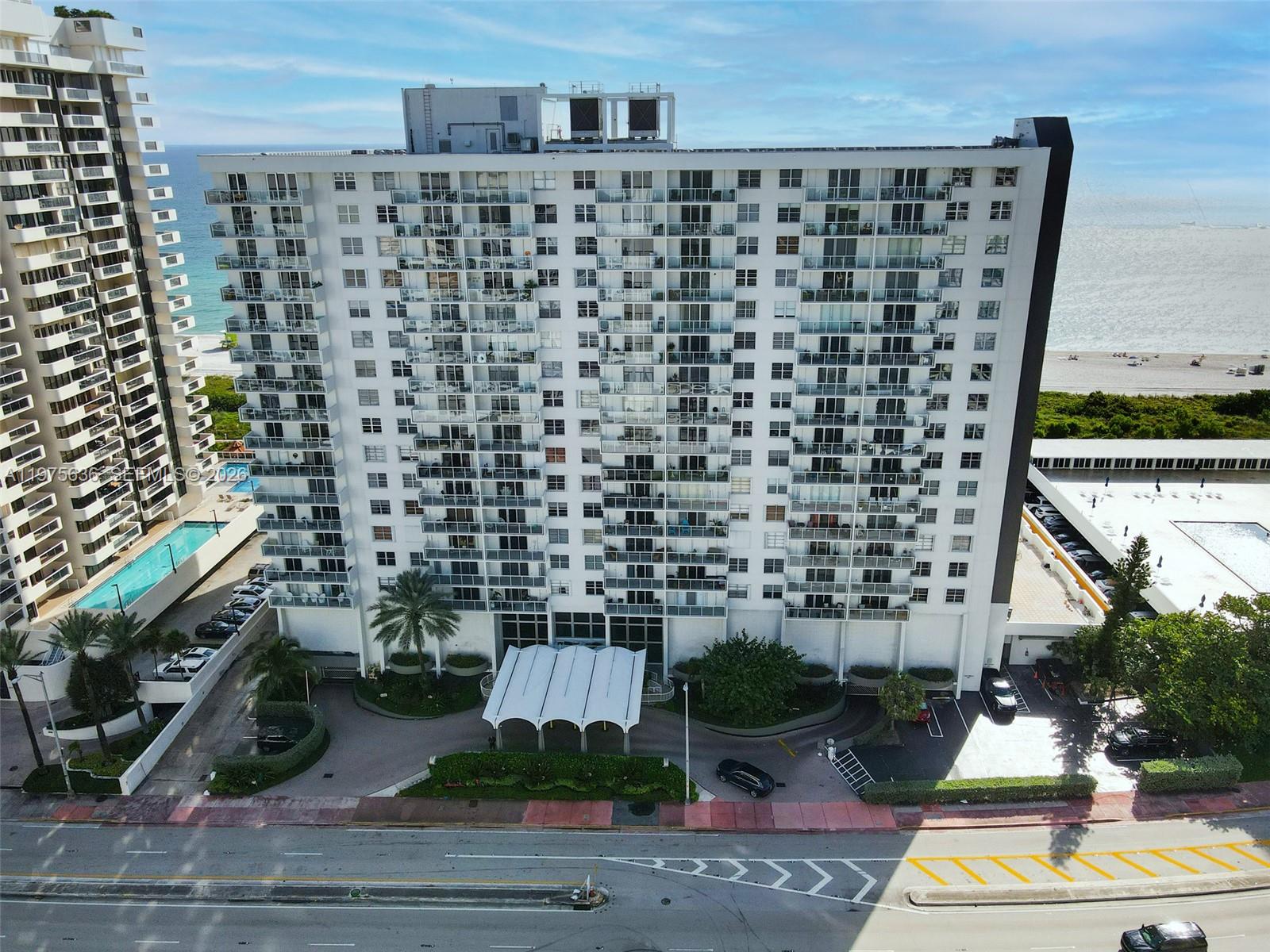 An aerial view shows a tall residential building with balconies, a pool, and a parking lot — 5701 Collins Ave # 803, Miami Beach FL 33140, MIAMI BEACH, FL