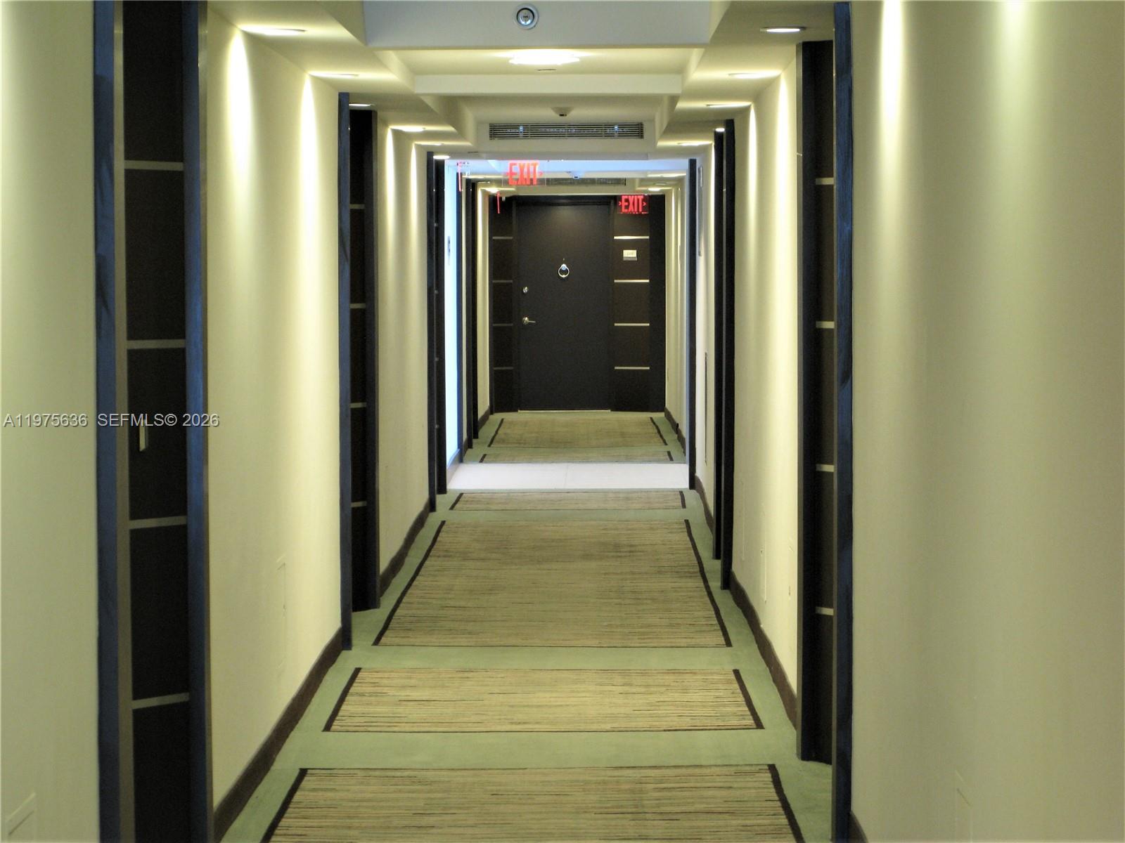 A long, narrow apartment hallway features beige walls, recessed lighting, and a patterned carpet runner — 5701 Collins Ave # 803, Miami Beach FL 33140, MIAMI BEACH, FL