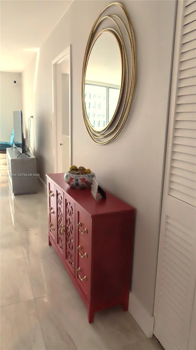 A red cabinet with gold hardware sits below a gold-framed mirror in a hallway — 5701 Collins Ave # 803, Miami Beach FL 33140, MIAMI BEACH, FL