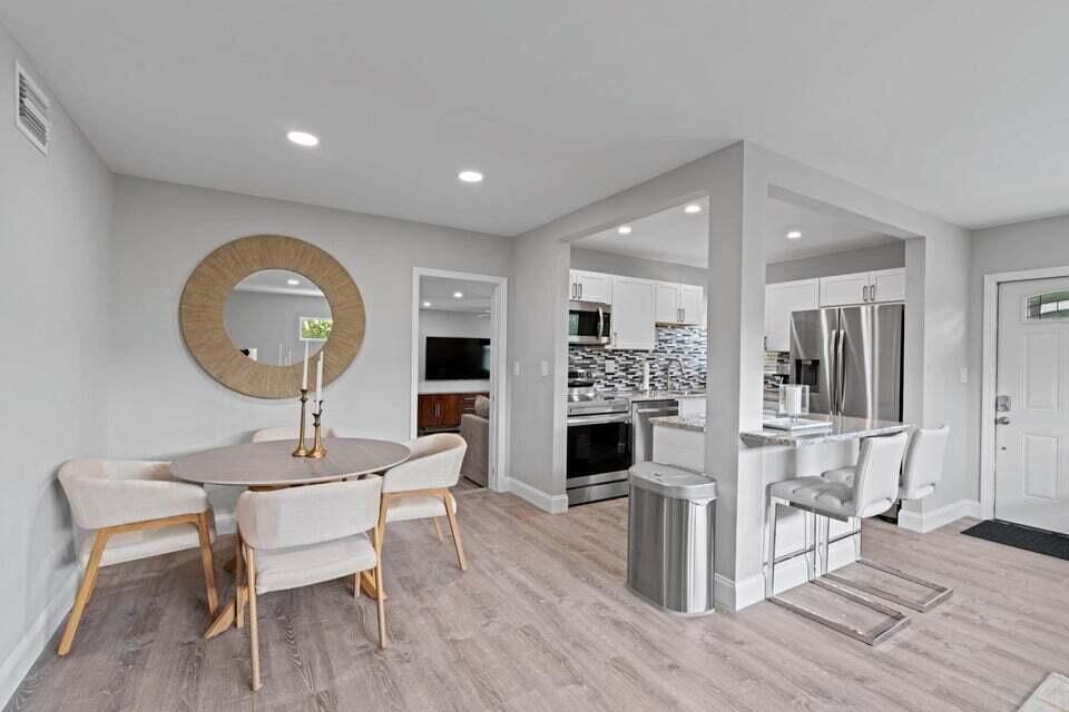 A dining area with a round table and mirror adjacent to a kitchen with bar seating — 2312 Spanish Trail, Delray Beach FL 33483, DELRAY BEACH, FL