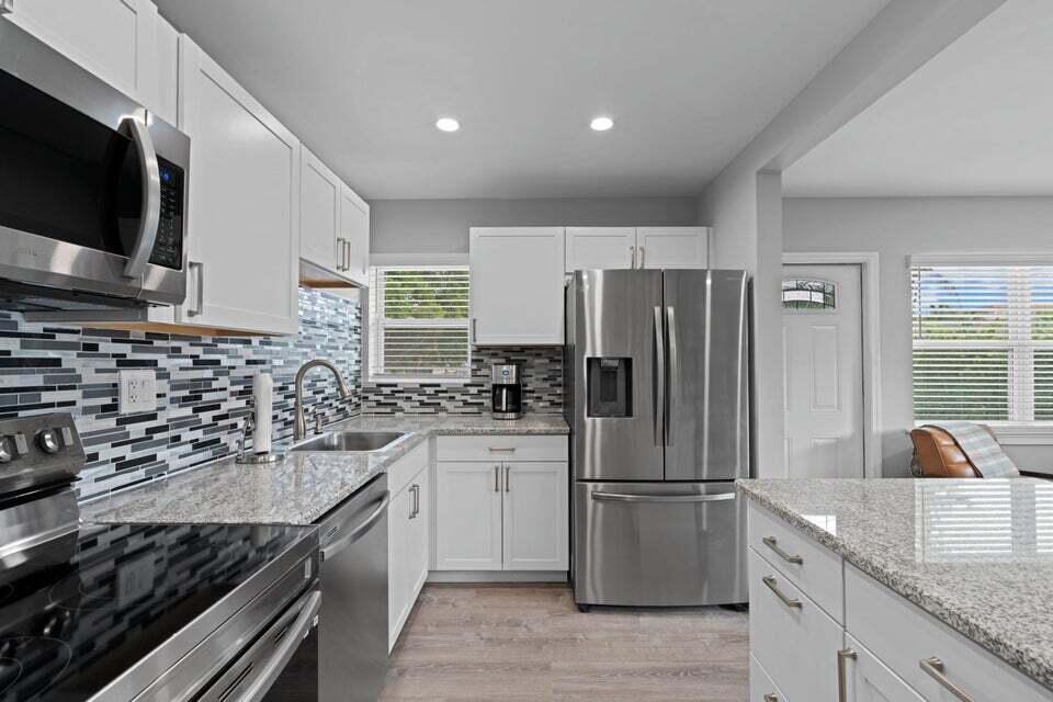 A kitchen features white cabinets, granite countertops, stainless steel appliances, and a mosaic tile backsplash — 2312 Spanish Trail, Delray Beach FL 33483, DELRAY BEACH, FL