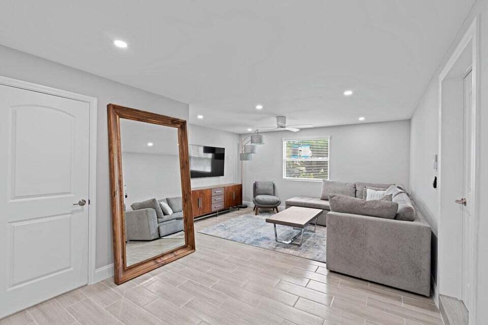 A living room features gray tile flooring, a large floor mirror, and a sectional sofa — 2312 Spanish Trail, Delray Beach FL 33483, DELRAY BEACH, FL