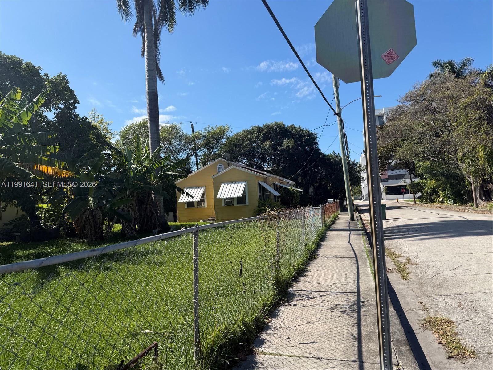 A yellow house sits behind a chain-link fence next to a sidewalk and street — 1234 NW 9th Ave, Miami FL 33136, MIAMI, FL