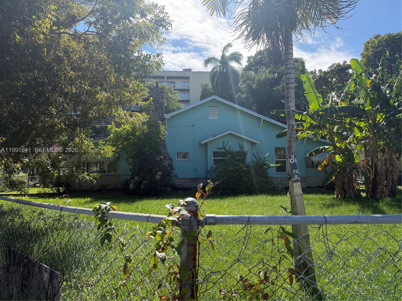 A light blue house with a stone chimney sits behind a chain-link fence — 1234 NW 9th Ave, Miami FL 33136, MIAMI, FL