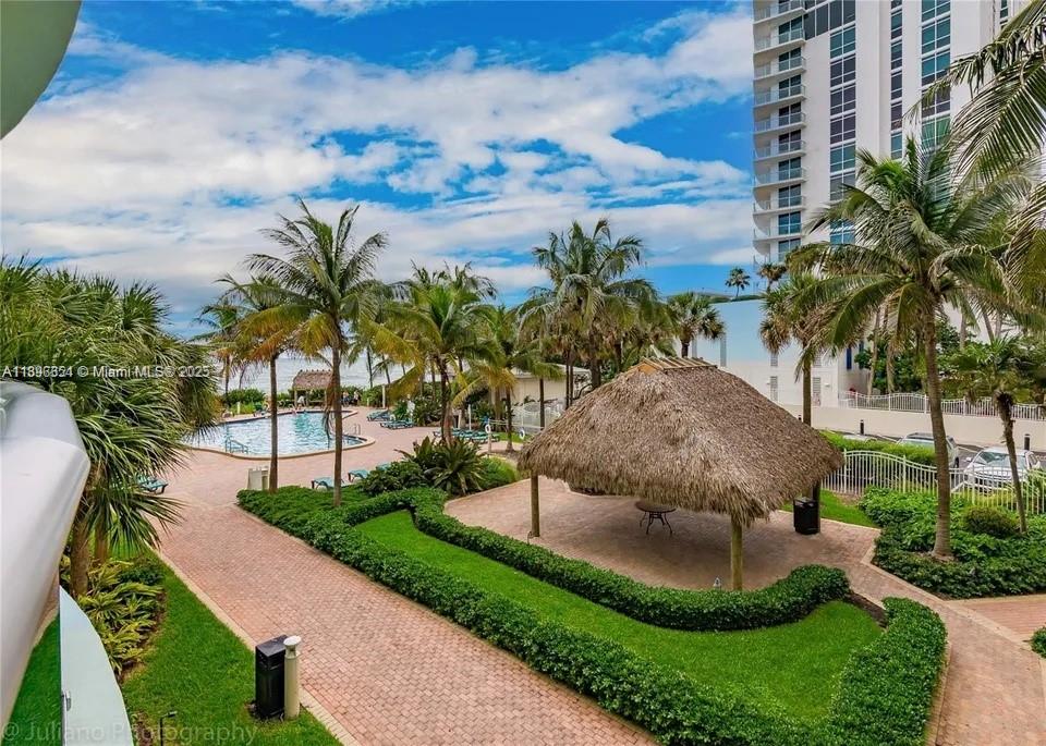 An outdoor view of a swimming pool, a thatched-roof gazebo, and palm trees — 3901 S Ocean Dr # 2H, Hollywood FL 33019, HOLLYWOOD, FL