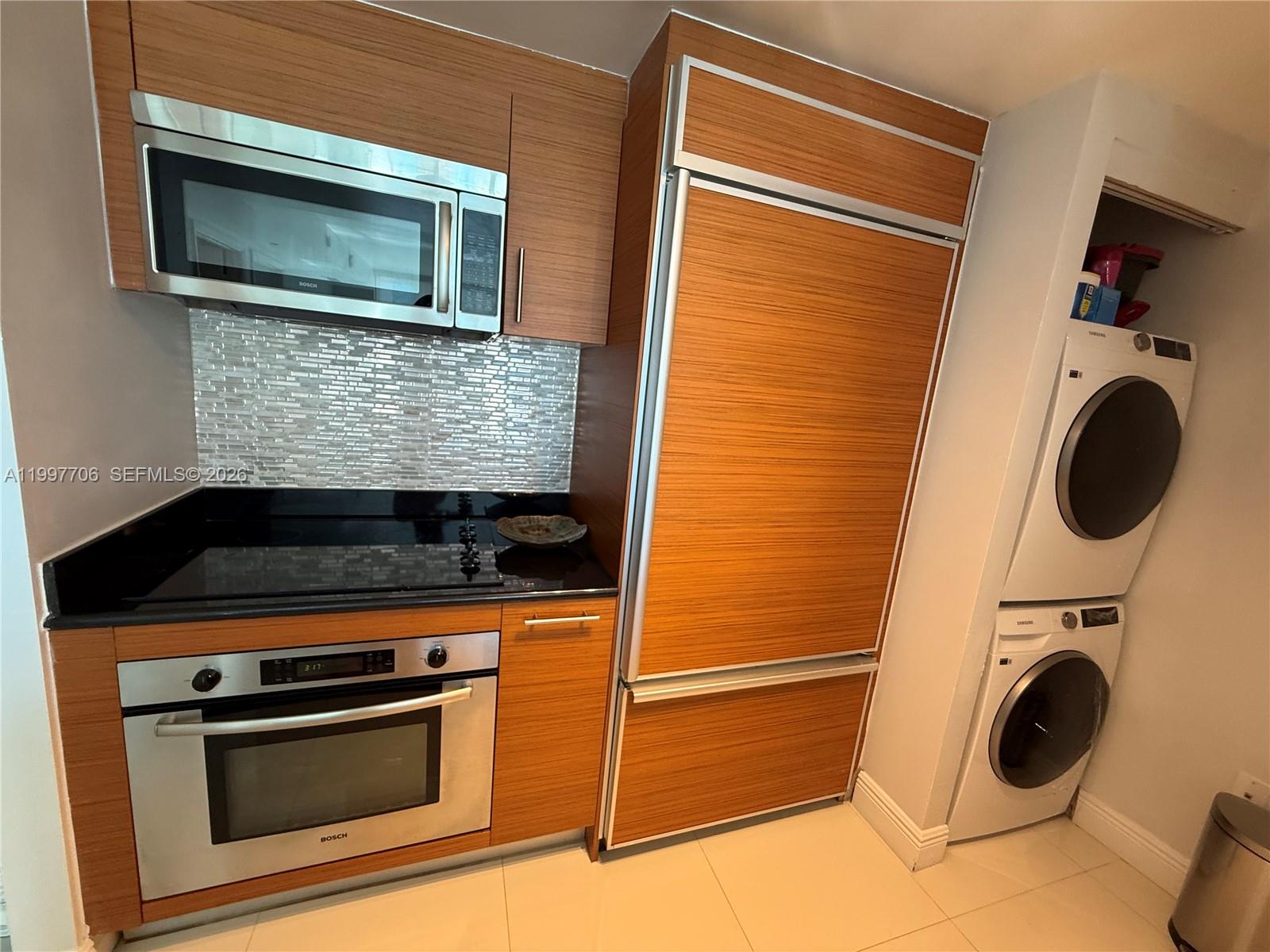 A kitchen features wood-paneled cabinetry, stainless steel Bosch appliances, and a stacked washer and dryer — 50 Biscayne Blvd # 1907, Miami FL 33132, MIAMI, FL