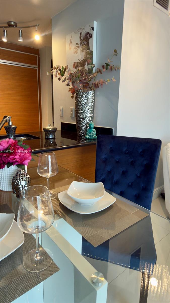 A dining area features a glass table, blue tufted chairs, and a decorative silver vase — 50 Biscayne Blvd # 1907, Miami FL 33132, MIAMI, FL