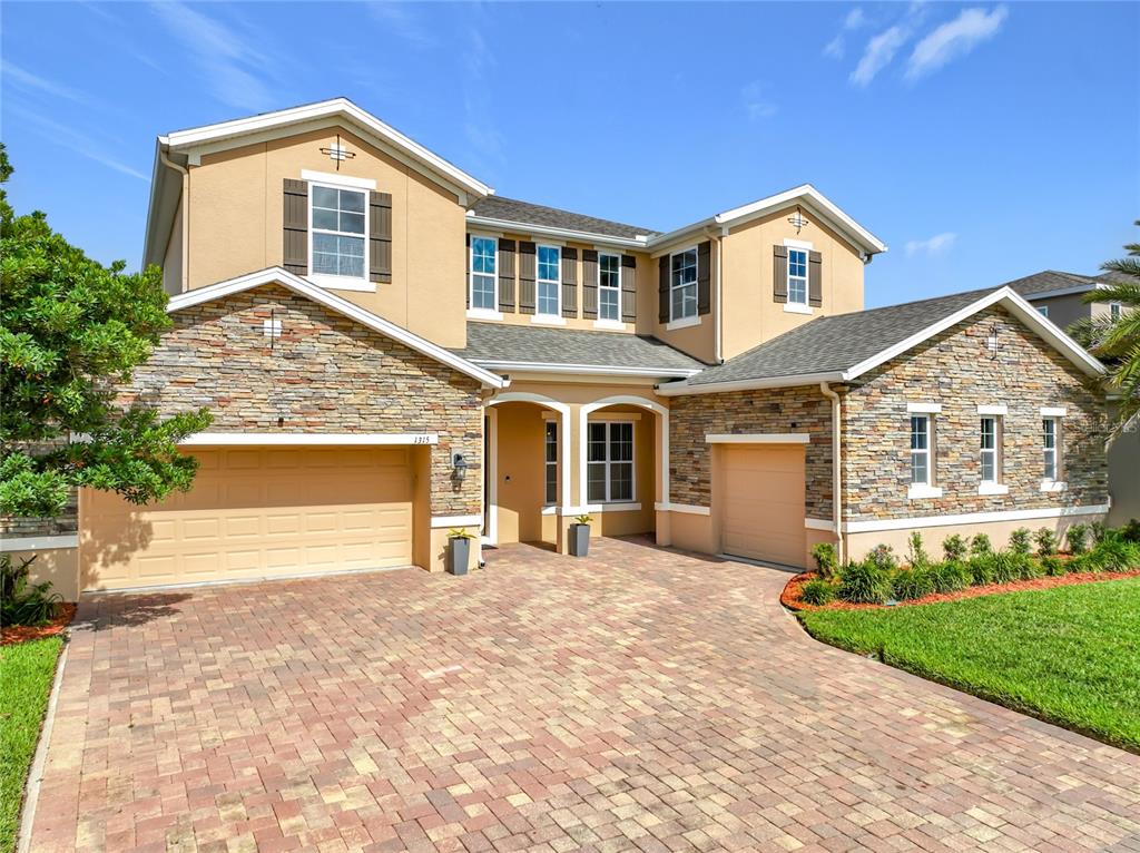 A two-story suburban house with a stone facade, tan stucco, and a brick paver driveway — 1315 DUSTY PINE DRIVE, APOPKA, FL