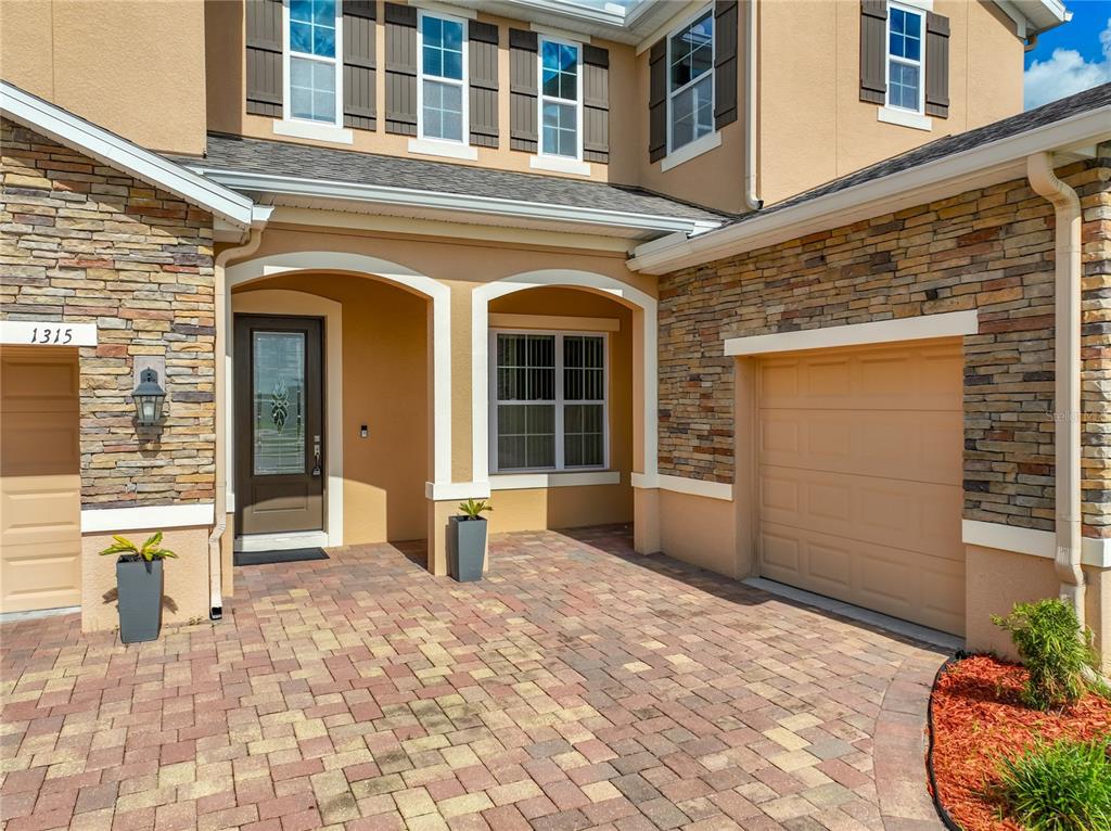 The exterior of a two-story home features stone veneer, a paver driveway, and a garage — 1315 DUSTY PINE DRIVE, APOPKA, FL