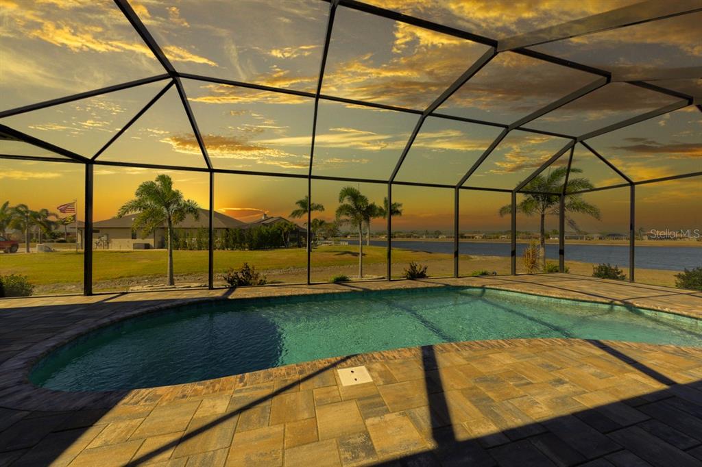 A swimming pool sits inside a screened lanai overlooking a lake at sunset — 25364 SAINT HELENA LANE, PUNTA GORDA, FL