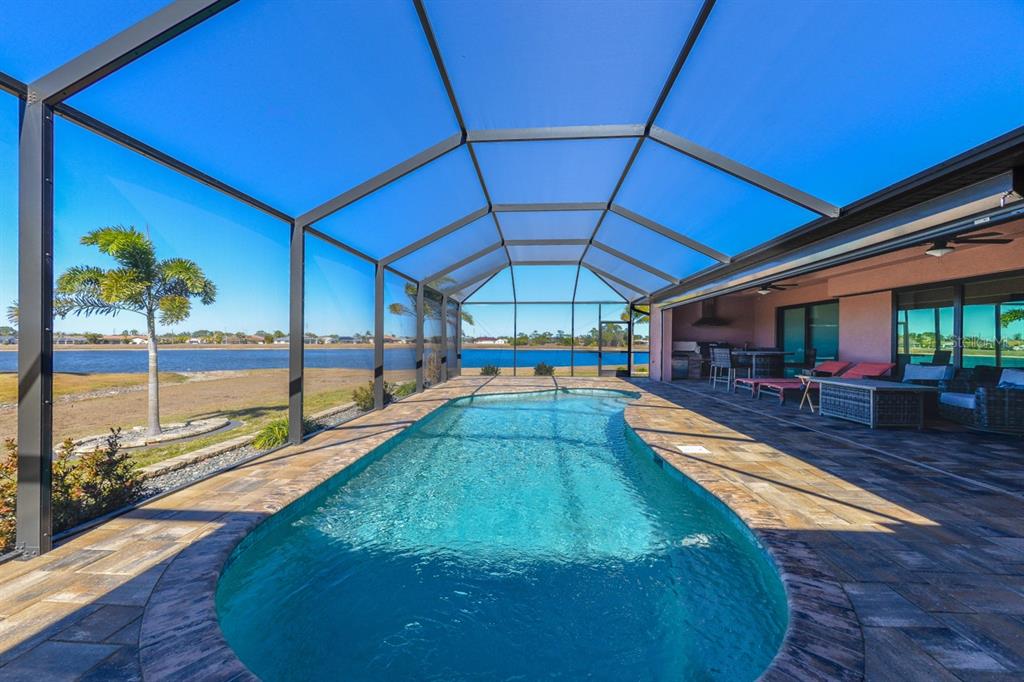 A swimming pool sits inside a screened-in lanai overlooking a lake and grassy yard — 25364 SAINT HELENA LANE, PUNTA GORDA, FL
