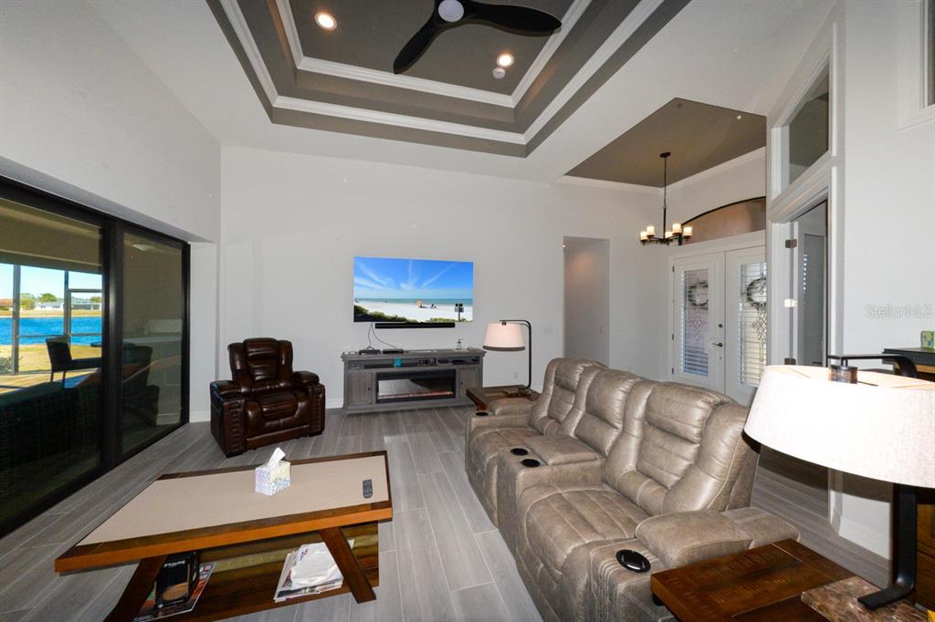A living room features a tray ceiling, tile flooring, a fireplace console, and sliding glass doors — 25364 SAINT HELENA LANE, PUNTA GORDA, FL