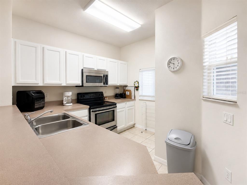 A kitchen features white cabinets, stainless steel appliances, a double sink, and beige countertops — 4558 ADA LANE, KISSIMMEE, FL