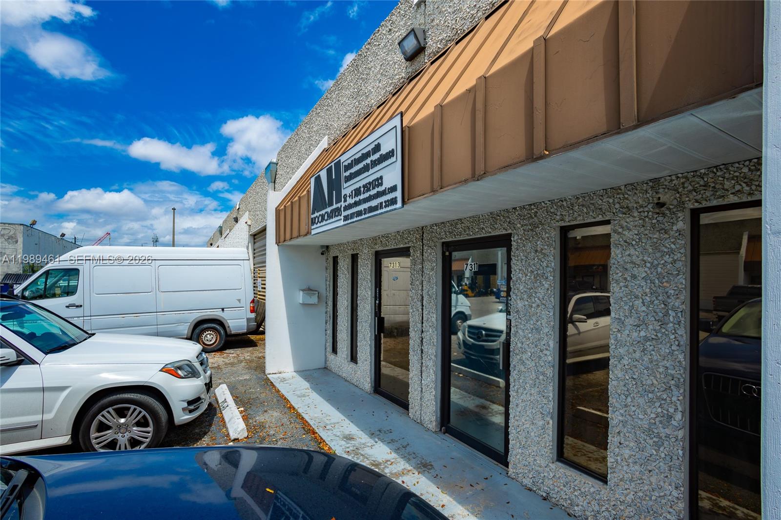 The exterior of a commercial building features a textured facade, glass doors, and parked vehicles — 7313 NW 56th St # 7313, Miami FL 33166, MIAMI, FL