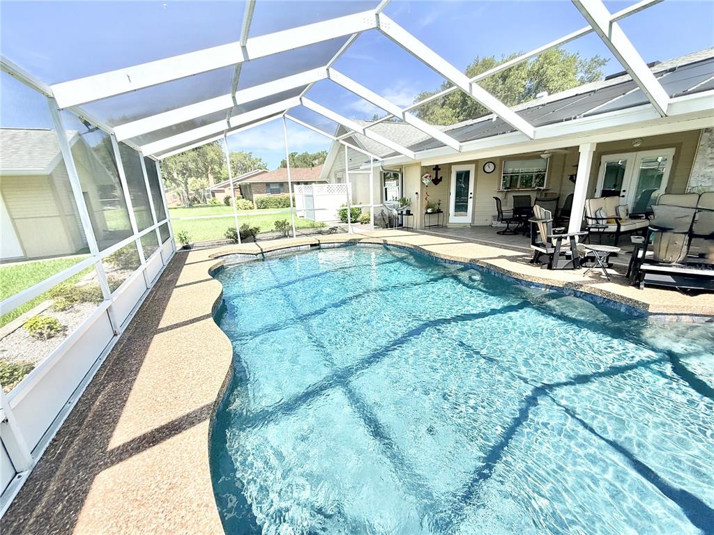 A swimming pool with a screen enclosure sits on a patio next to a house — 305 W DELAWARE STREET, TAVARES, FL