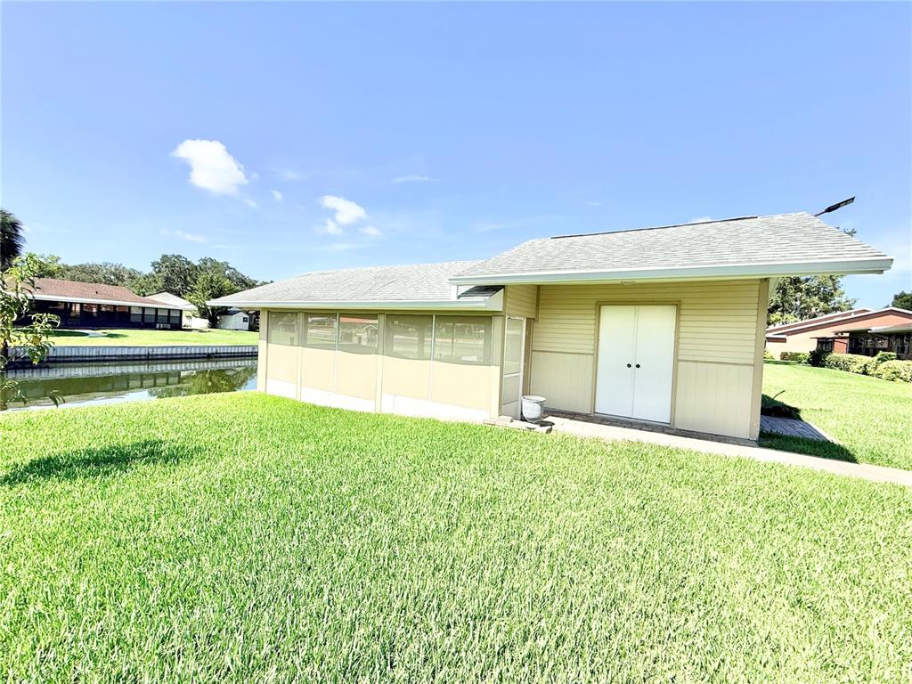 A tan house with a screened-in porch and double doors sits beside a canal — 305 W DELAWARE STREET, TAVARES, FL