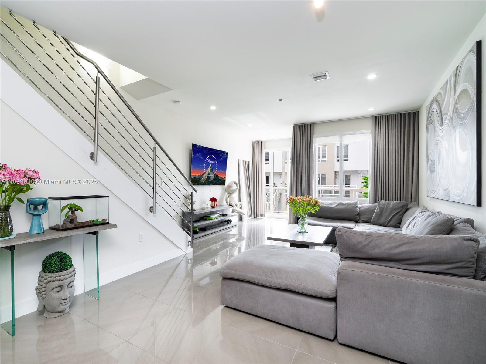 A modern living room features a grey sectional sofa, a staircase, and tile flooring — 10245 NW 63rd Ter # 206, Doral FL 33178, DORAL, FL