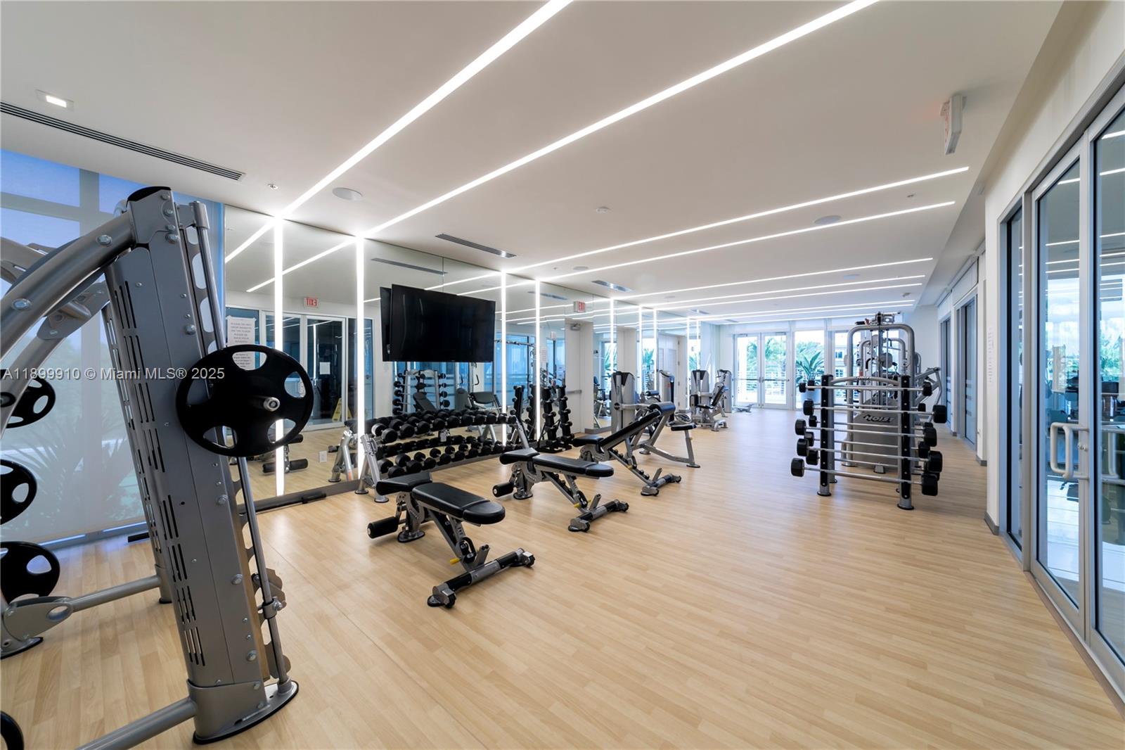 A modern gym features light wood flooring, mirrored walls, and various strength training equipment — 10245 NW 63rd Ter # 206, Doral FL 33178, DORAL, FL