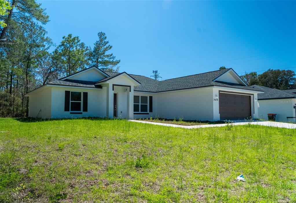 A single-story house with a white exterior, dark roof, and attached garage sits on grass — 5670 SW 161ST PLACE, OCALA, FL
