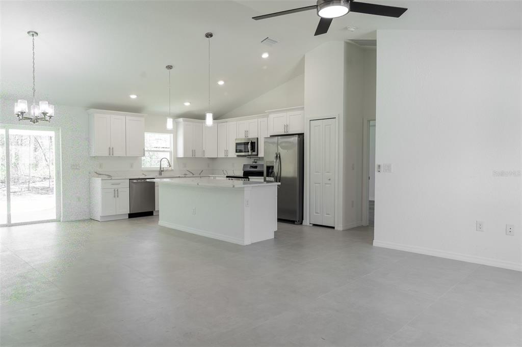 A modern kitchen features white cabinetry, a central island, stainless steel appliances, and tile flooring — 5670 SW 161ST PLACE, OCALA, FL