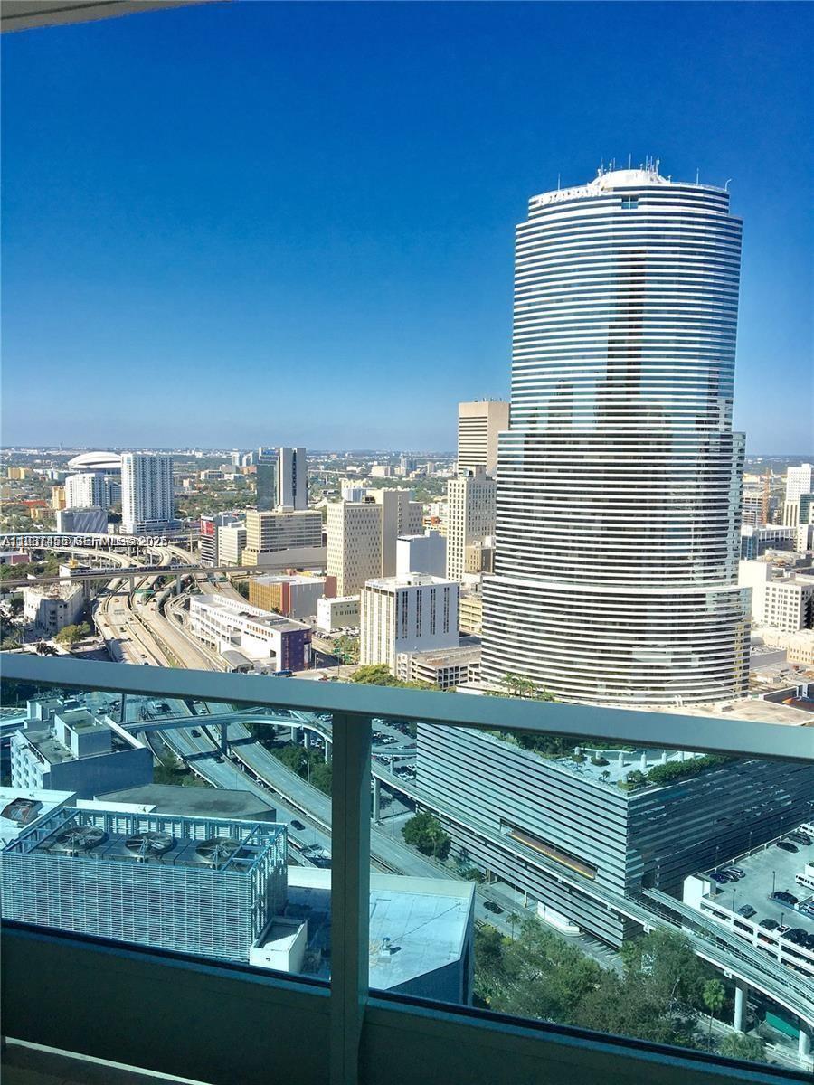 A high-angle view of a city skyline featuring a prominent cylindrical skyscraper and highway overpasses — 200 Biscayne Boulevard Way # 3712, Miami FL 33131, MIAMI, FL