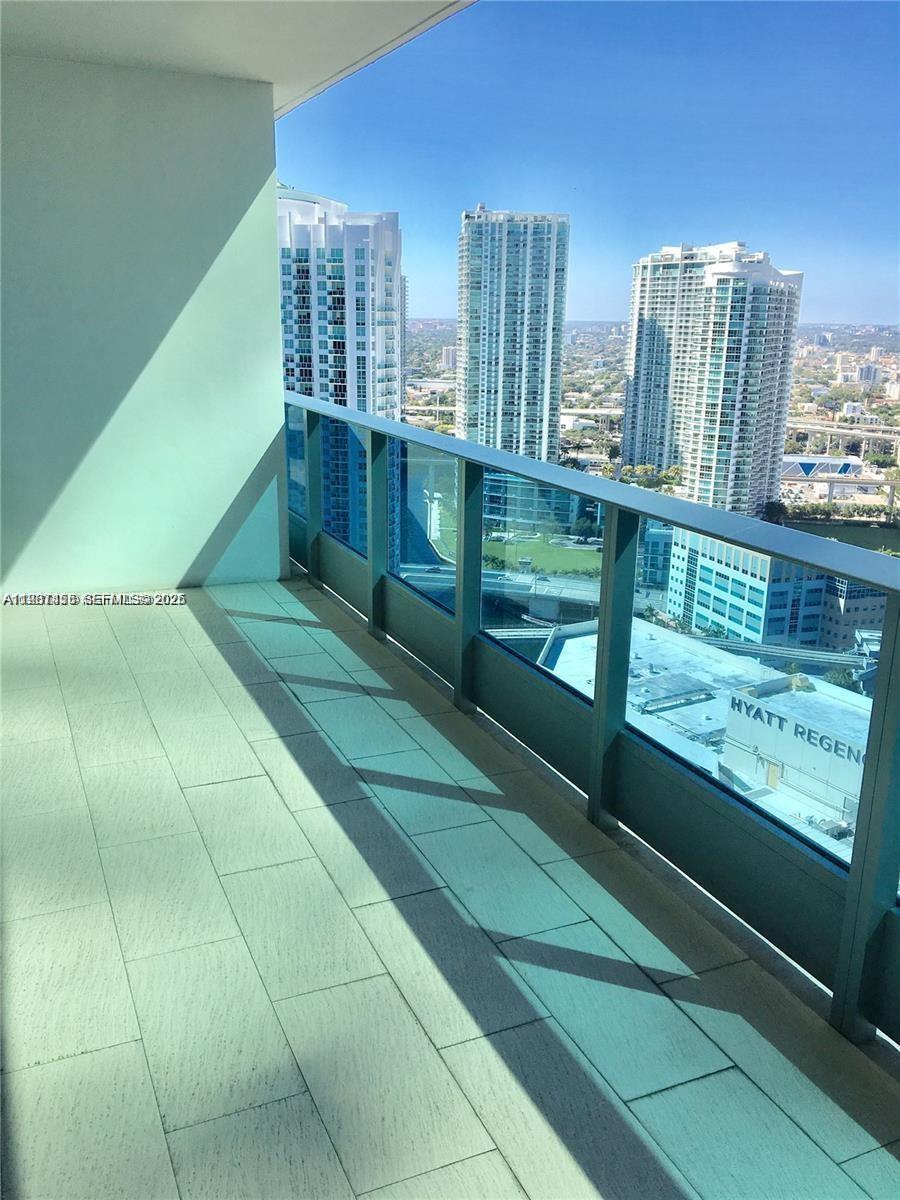 A high-rise balcony features light-colored tile flooring and a glass railing overlooking city buildings — 200 Biscayne Boulevard Way # 3712, Miami FL 33131, MIAMI, FL