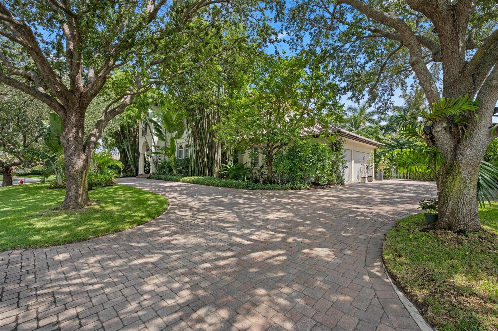 A paved driveway leads to a two-story house surrounded by mature trees and lush landscaping — 4699 Gleneagles Drive, Boynton Beach FL 33436, BOYNTON BEACH, FL