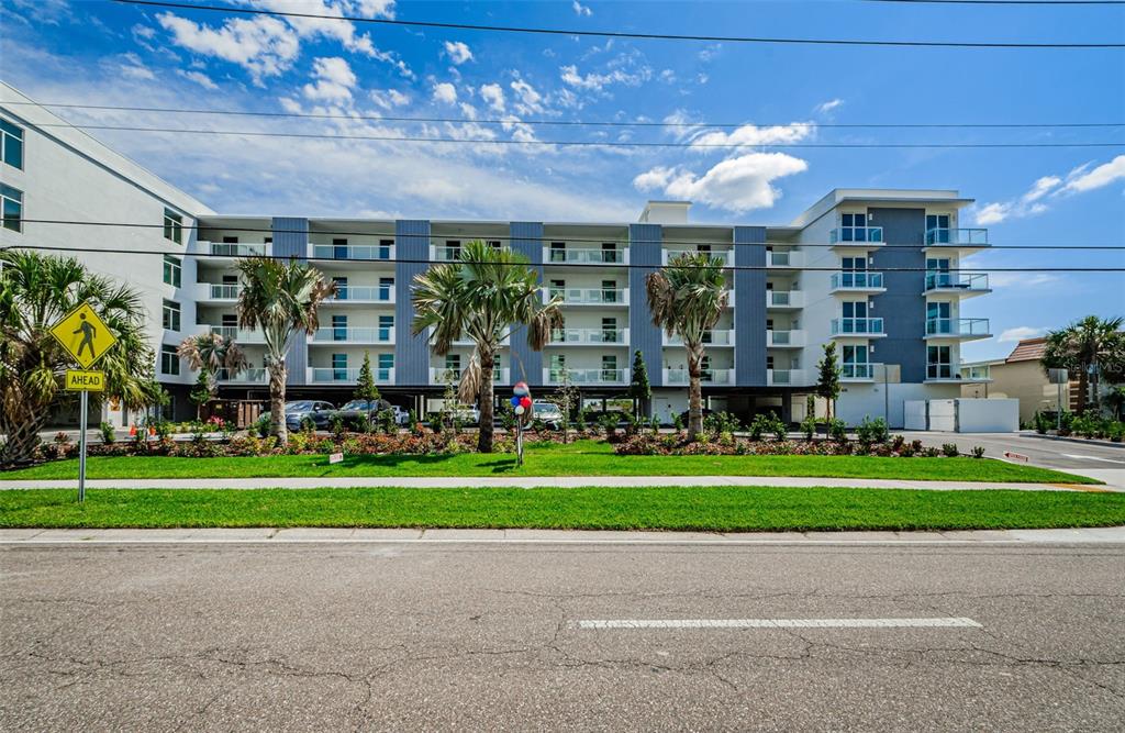 A multi-story apartment building with balconies stands behind a grassy lawn and palm trees — 415 ISLAND WAY UNIT 509, CLEARWATER BEACH, FL