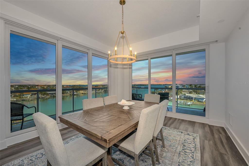 A dining room with a wooden table, upholstered chairs, and floor-to-ceiling windows overlooking water — 415 ISLAND WAY UNIT 509, CLEARWATER BEACH, FL