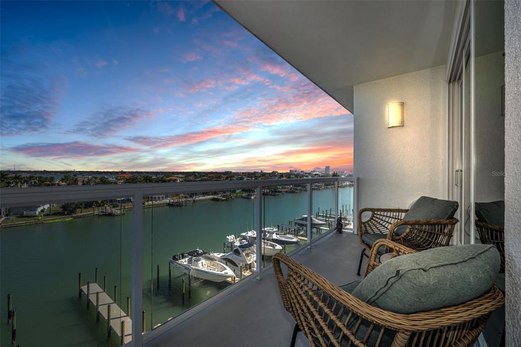 A balcony with wicker chairs overlooks a canal filled with boats at sunset — 415 ISLAND WAY UNIT 509, CLEARWATER BEACH, FL