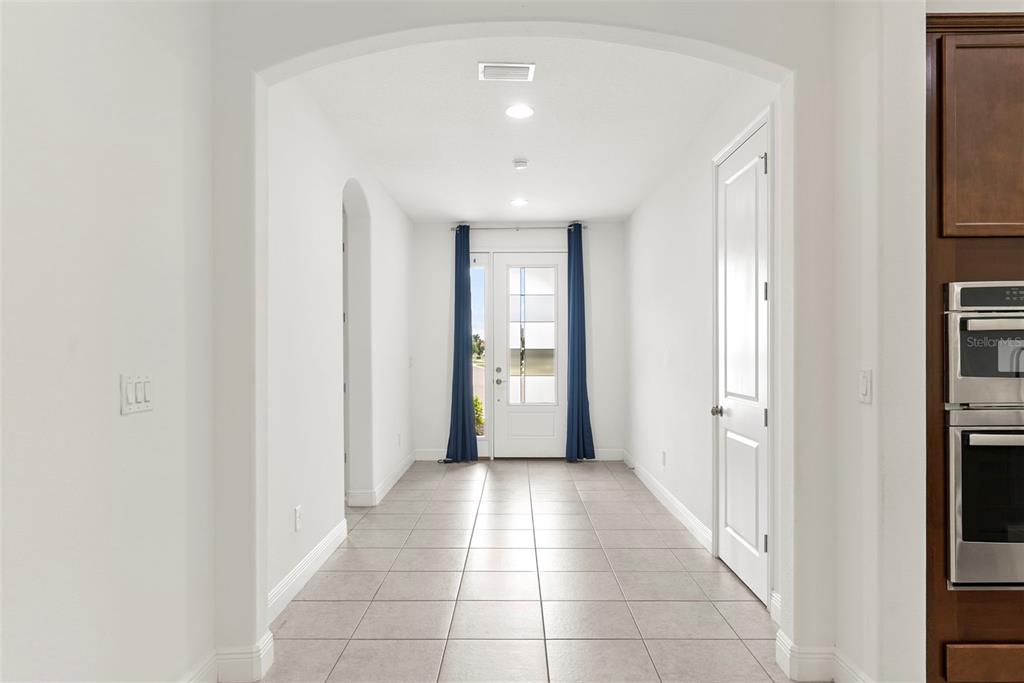 A tiled hallway leads to a front door framed by blue curtains under an archway — 3918 GAVIOTA DRIVE, SUN CITY CENTER, FL