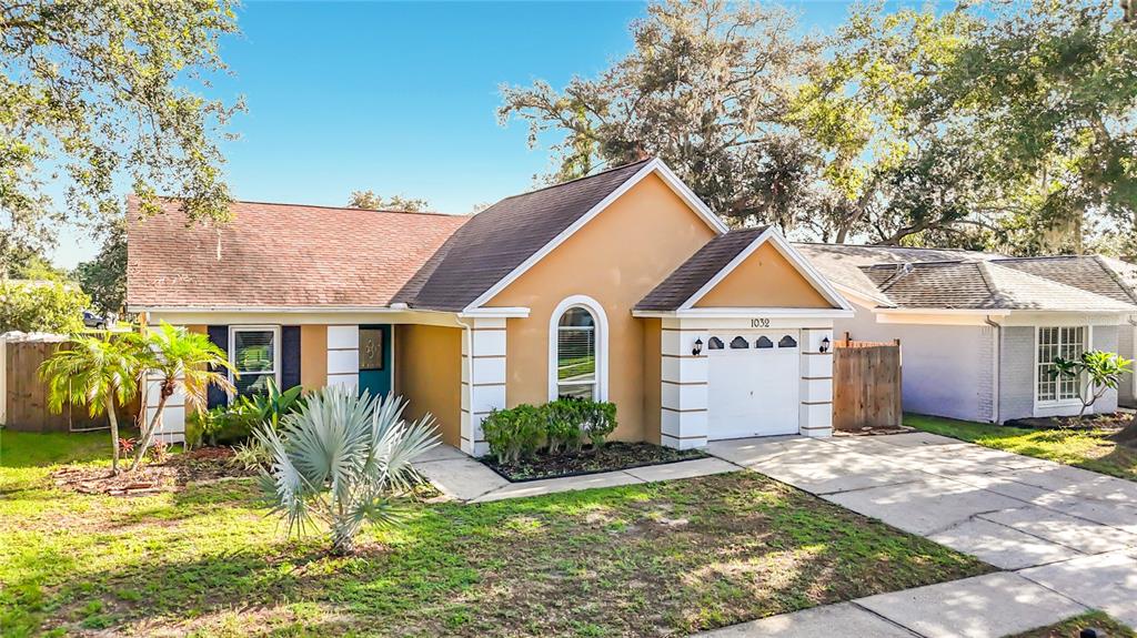 A tan, single-story house with a white garage, arched window, and a palm tree in front — 1032 HARDWOOD DRIVE, VALRICO, FL