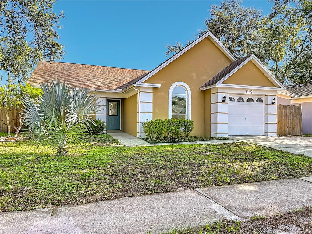 A single-story house with a tan exterior, white trim, a garage, and a front lawn — 1032 HARDWOOD DRIVE, VALRICO, FL