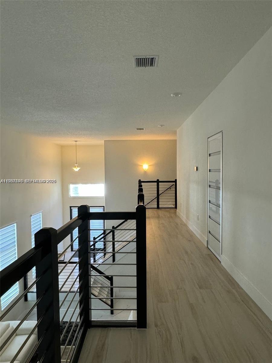 An interior view shows a hallway with light wood flooring and a black metal railing — 10376 NW 76th Ter, Doral FL 33178, DORAL, FL