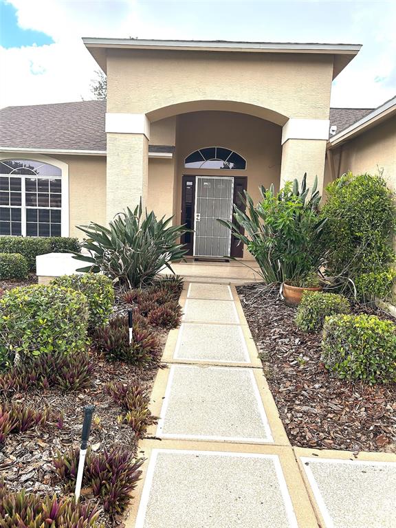 A concrete walkway leads to the front entrance of a house with a stucco exterior — 18702 BELLEVISTA COURT, HUDSON, FL