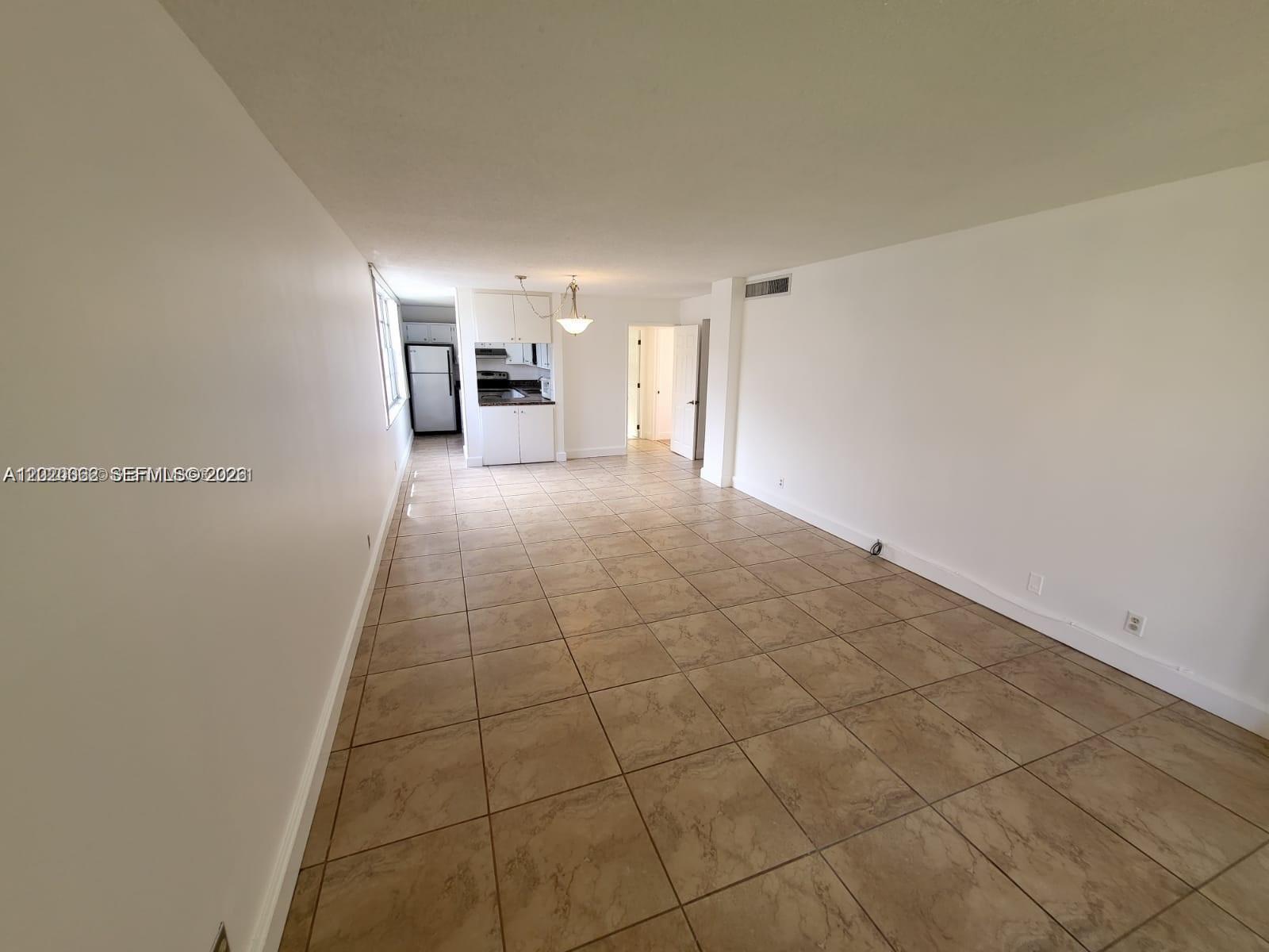 An open-concept living and dining area features beige tile flooring and a small kitchen — 9440 Live Oak Pl # 201, Davie FL 33324, DAVIE, FL